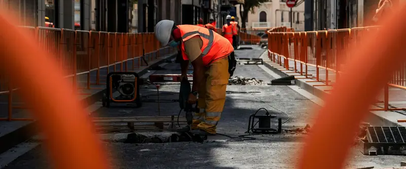 Un trabajador con casco y chaleco naranja hace obras en una calle de Alicante.