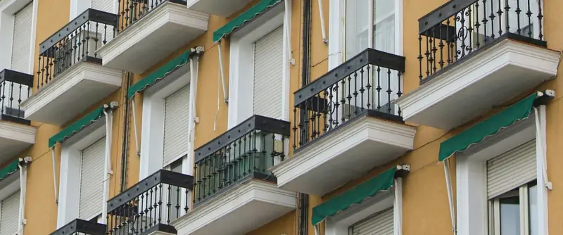 Fachada de un edificio de pisos con balcones y toldos verdes en Madrid.